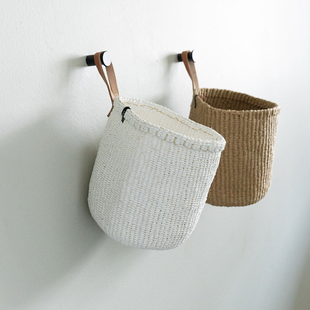 Two woven baskets, one white and one brown, hanging on a white wall.