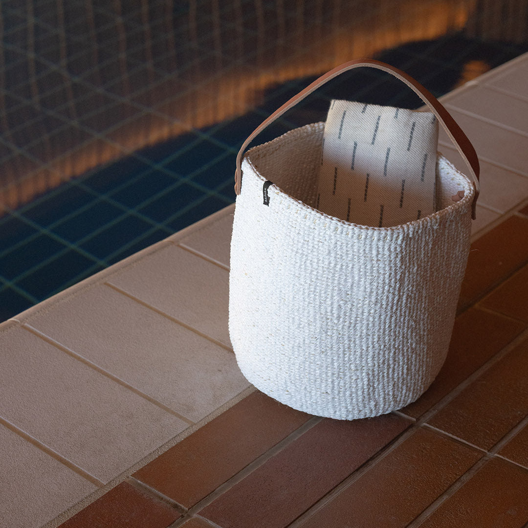 White woven basket with a handle on a tiled floor near a pool.