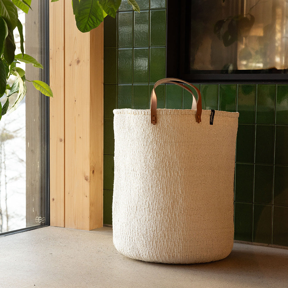 White woven basket with leather handles on a light floor.