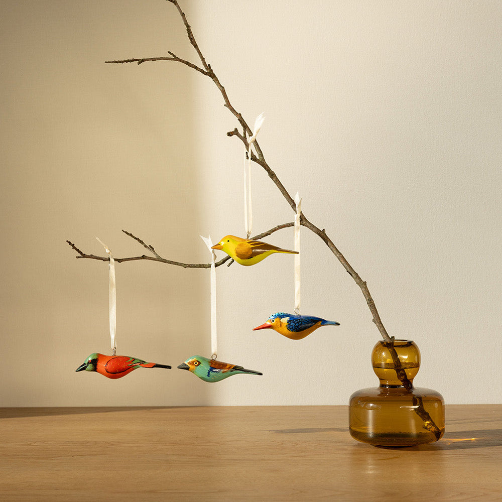 Decorative birds hanging from a branch in a vase on a wooden surface.
