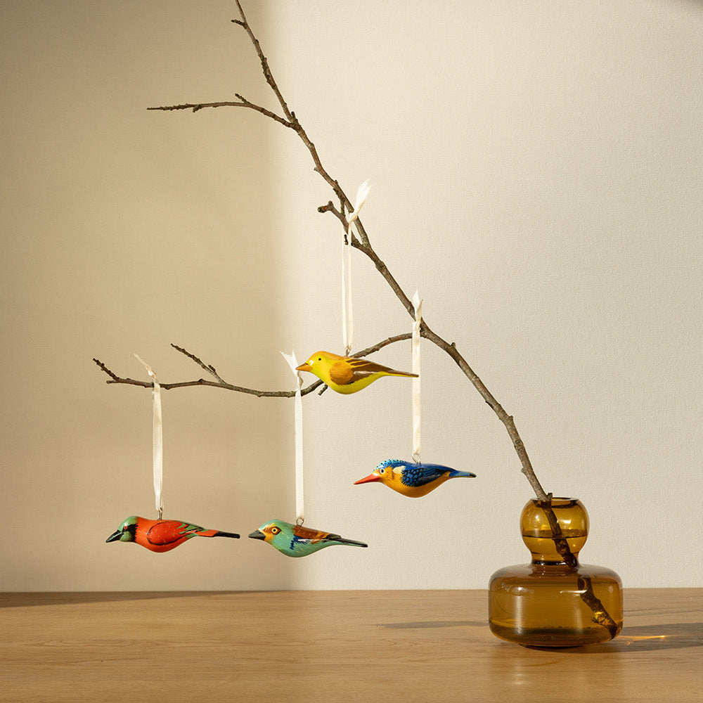 Decorative birds hanging from a branch in a vase on a wooden surface.