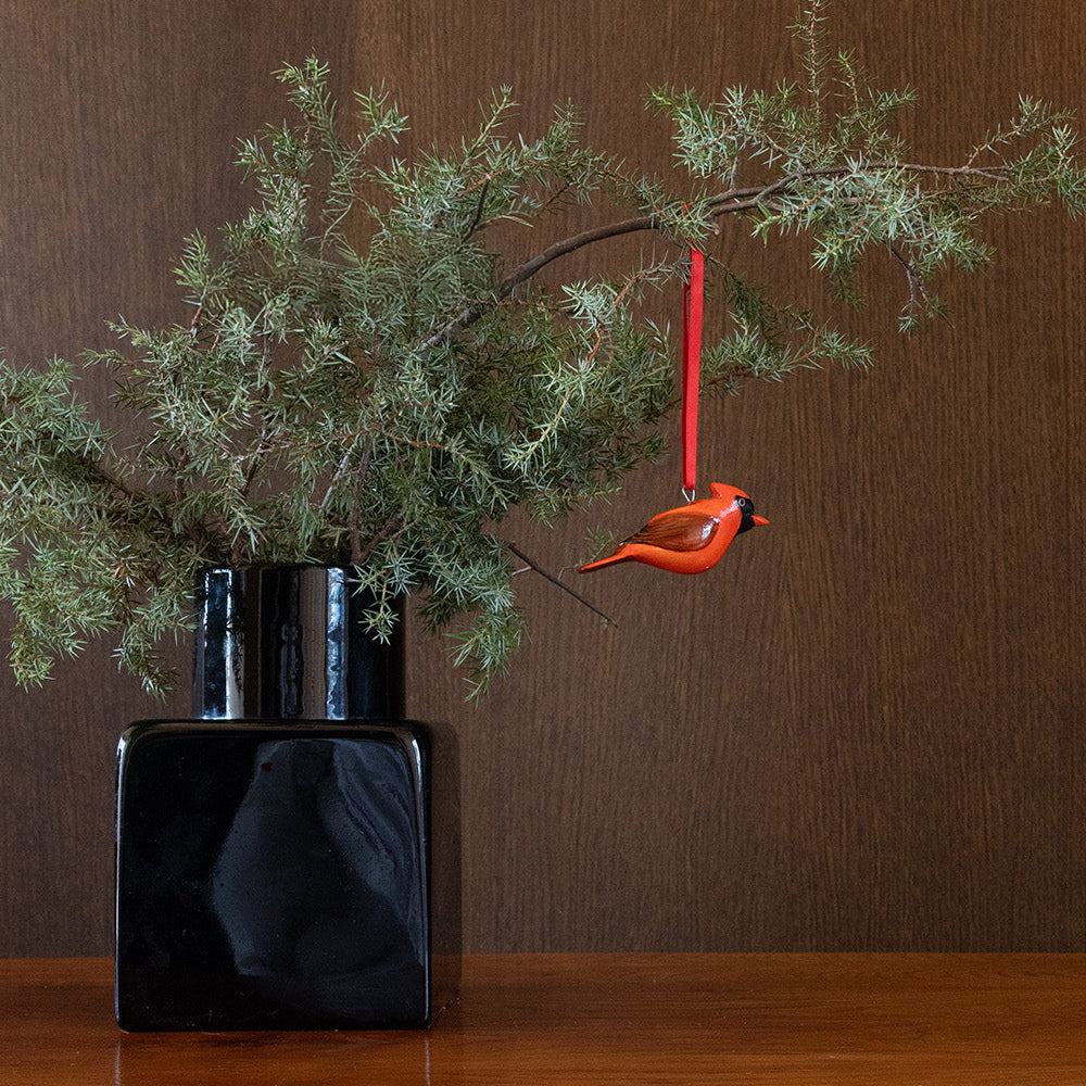 Decorative vase with greenery and a red bird ornament against a brown background