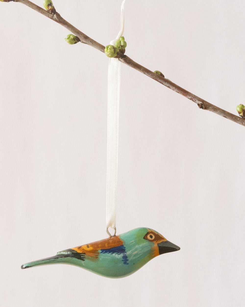 Decorative bird ornament hanging from a branch against a light background