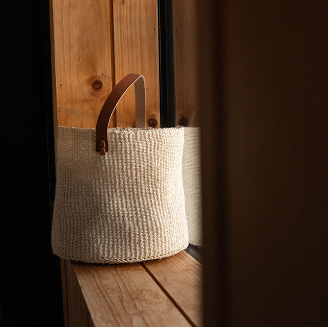 Textured woven basket with a wooden handle on a wooden surface.