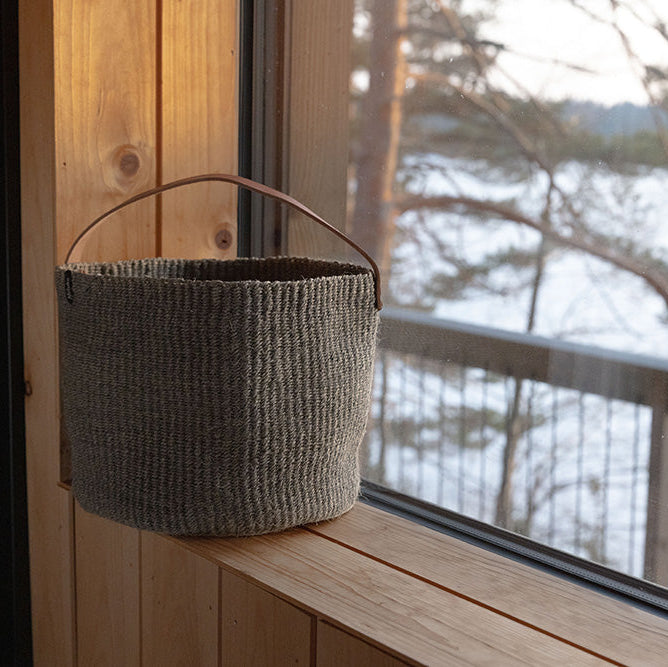 Woven basket hanging on a wooden ledge with a view of a lake and trees.
