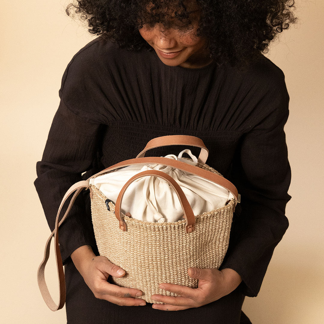 Person holding a woven basket with a beige interior against a beige background