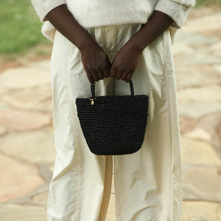 Person holding a black woven handbag outdoors on a stone path