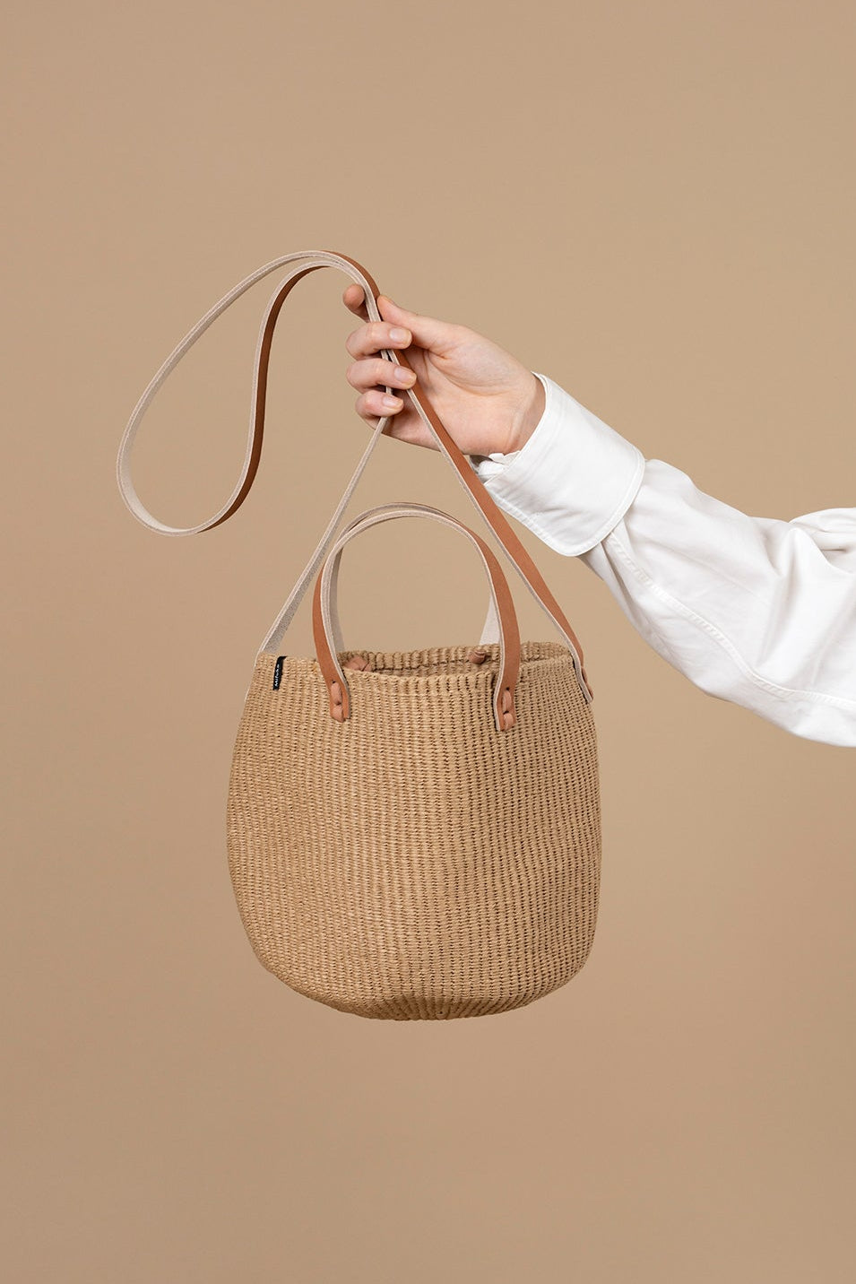 Hand holding a woven basket bag against a beige background