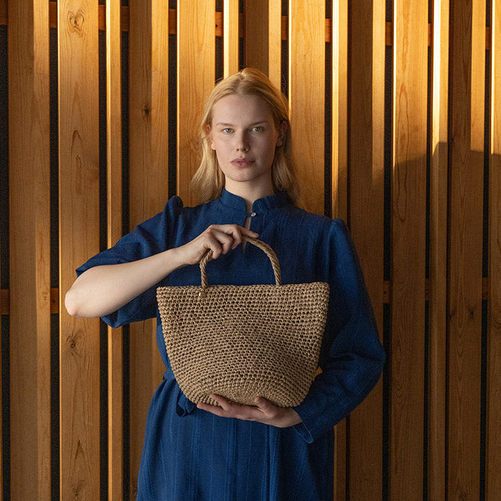 Woman holding a woven bag against a wooden slat background