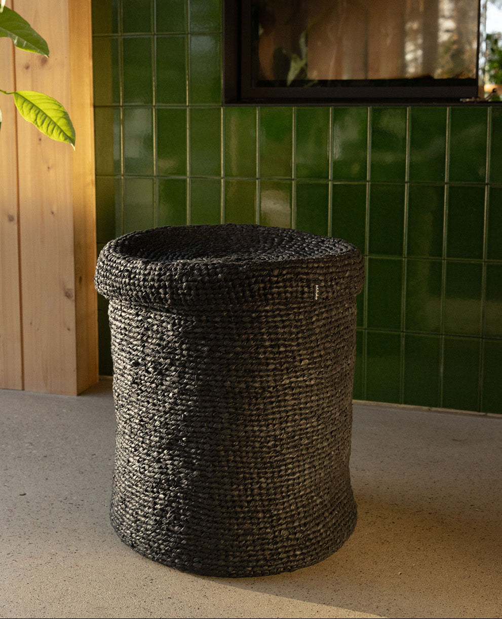 Woven basket on a concrete floor with green tiled wall and wooden panel in the background