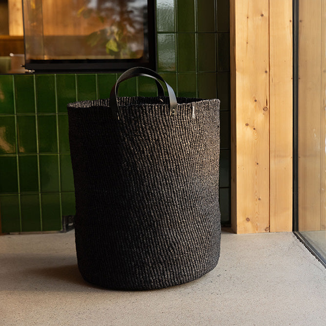 Black woven basket on a windowsill with a view of trees and water outside.