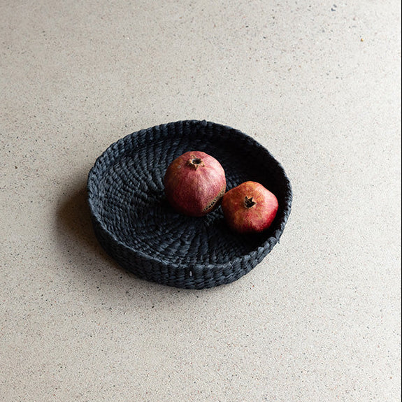 Black woven basket with two apples on a beige surface