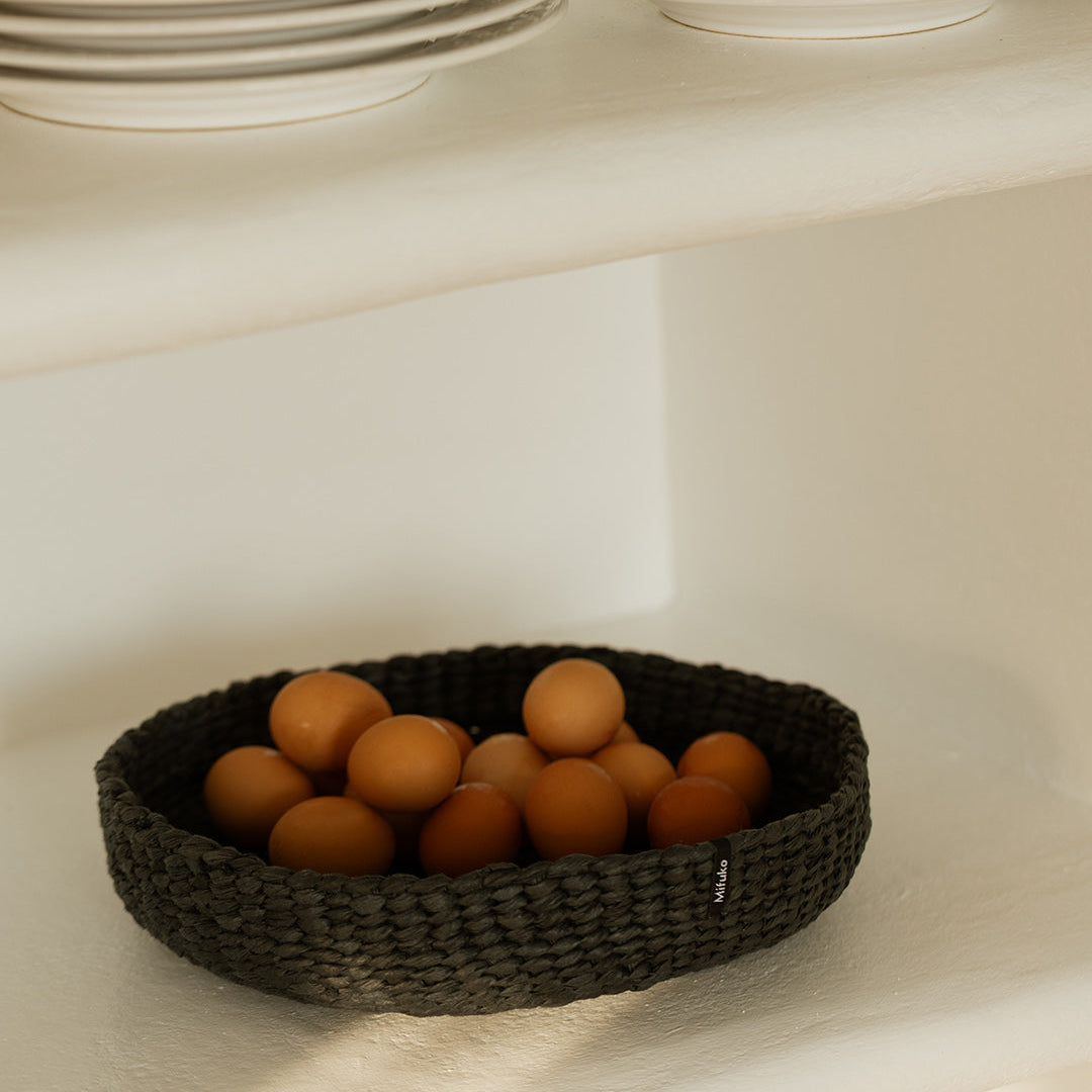 handwoven black basket with eggs on a white shelf