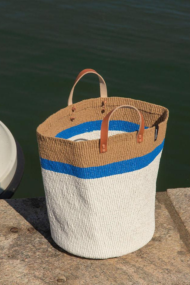 The Kiondo Market Basket with a striking top stripe in blue is a beautiful and practical accessory that combines traditional craftsmanship with modern design. Handwoven with care by skilled artisans, this large basket is made from a unique blend of FSC-certified paper and upcycled plastic, making it lightweight, durable, and environmentally conscious.
