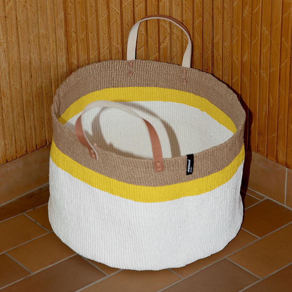 The Kiondo Floor Basket with a vibrant top stripe in yellow is a statement piece that combines style, functionality, and sustainability. Handwoven by skilled artisans, this extra-large basket is crafted from a unique blend of FSC-certified paper and upcycled plastic, making it lightweight yet durable.
