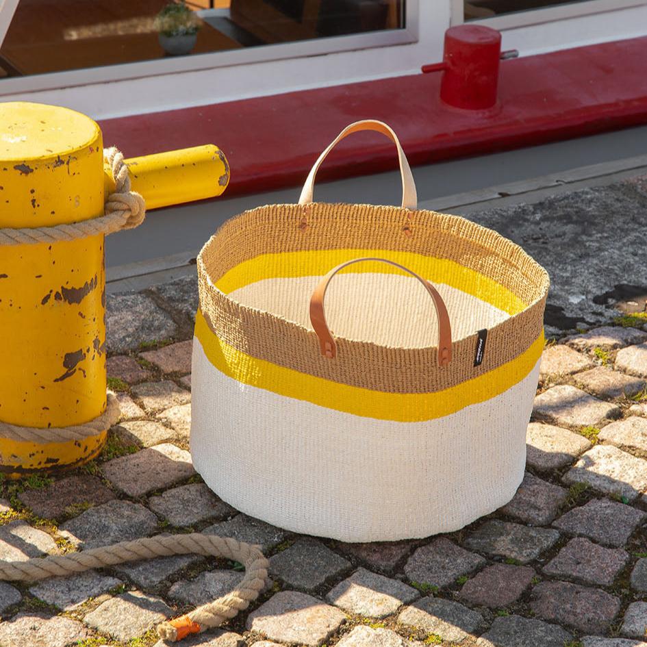 The Kiondo Floor Basket with a vibrant top stripe in yellow is a statement piece that combines style, functionality, and sustainability. Handwoven by skilled artisans, this extra-large basket is crafted from a unique blend of FSC-certified paper and upcycled plastic, making it lightweight yet durable.