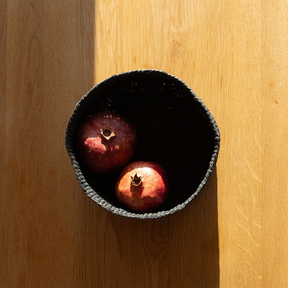 Two pomegranates in a black bowl on a wooden surface