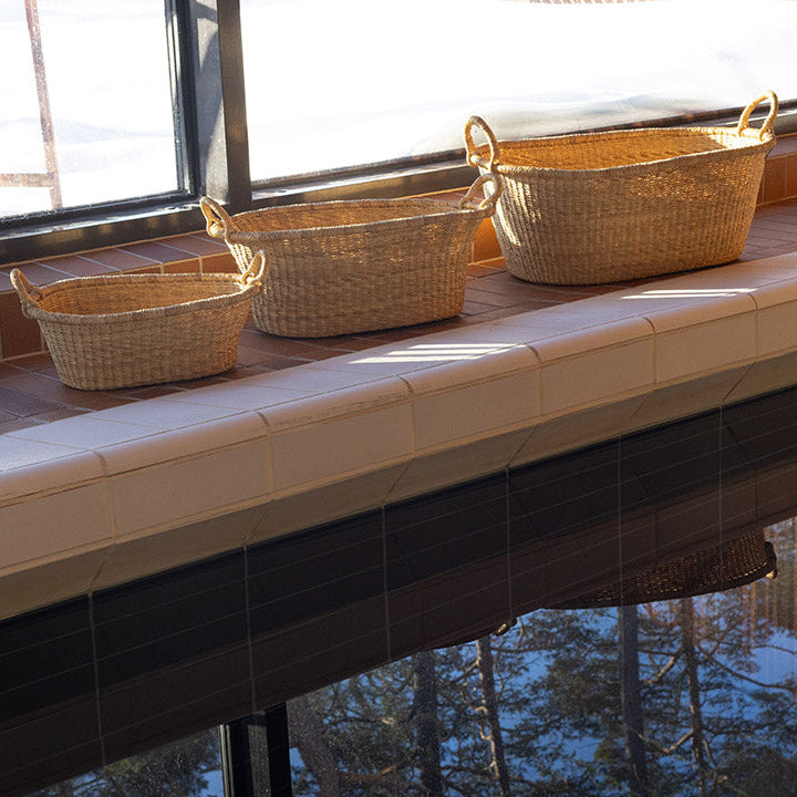 Three woven baskets on a tiled ledge by a window with a reflective surface below.