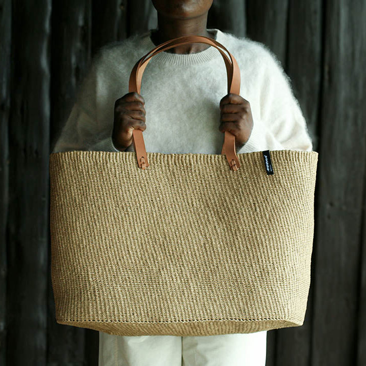 Person holding a handwoven bag with leather handles against a dark background paper fair trade