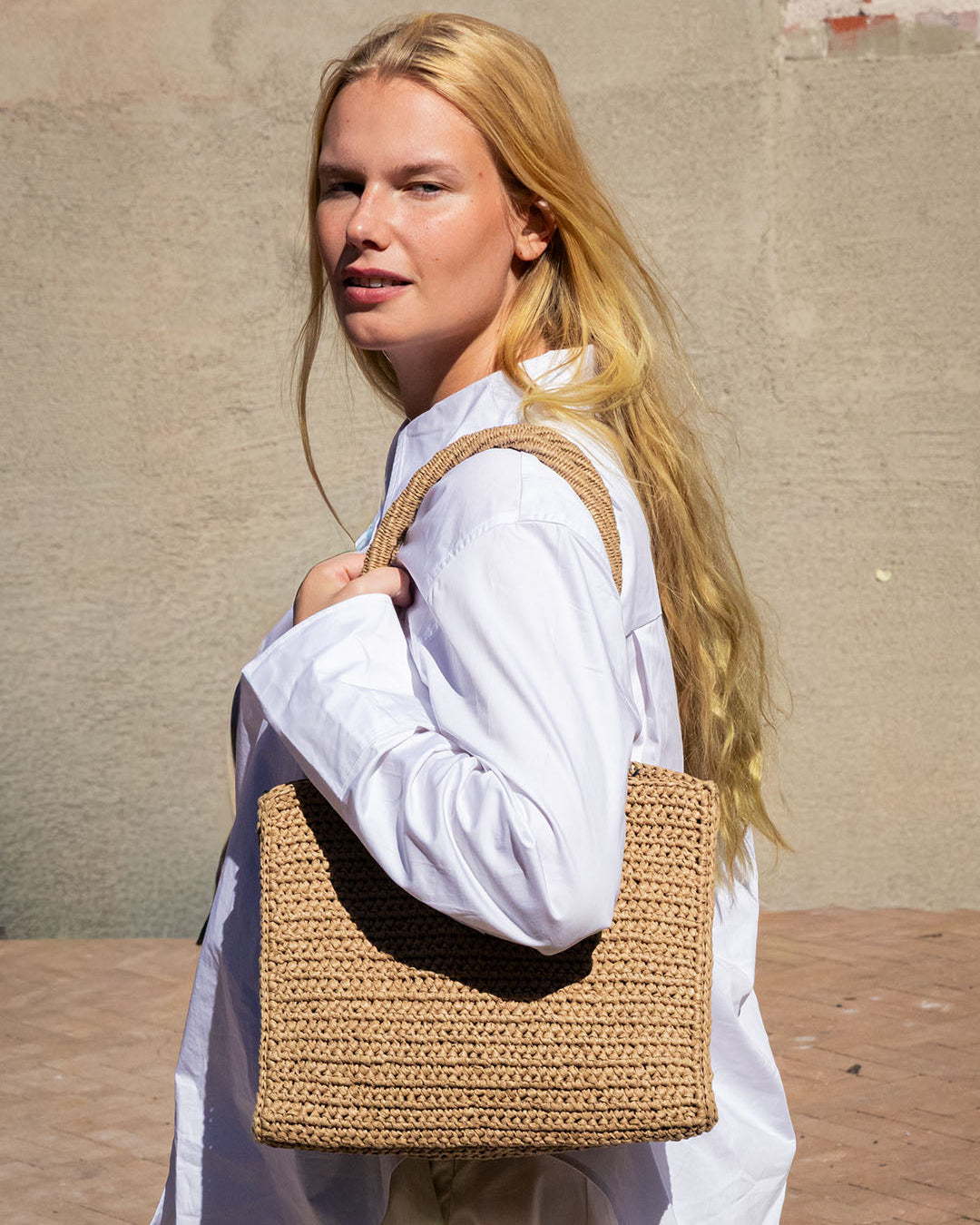 Woman holding a woven bag against a beige wall