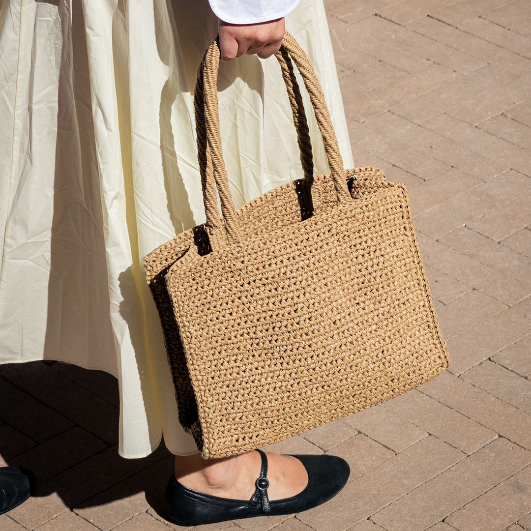 Person holding a woven handbag on a wooden floor
