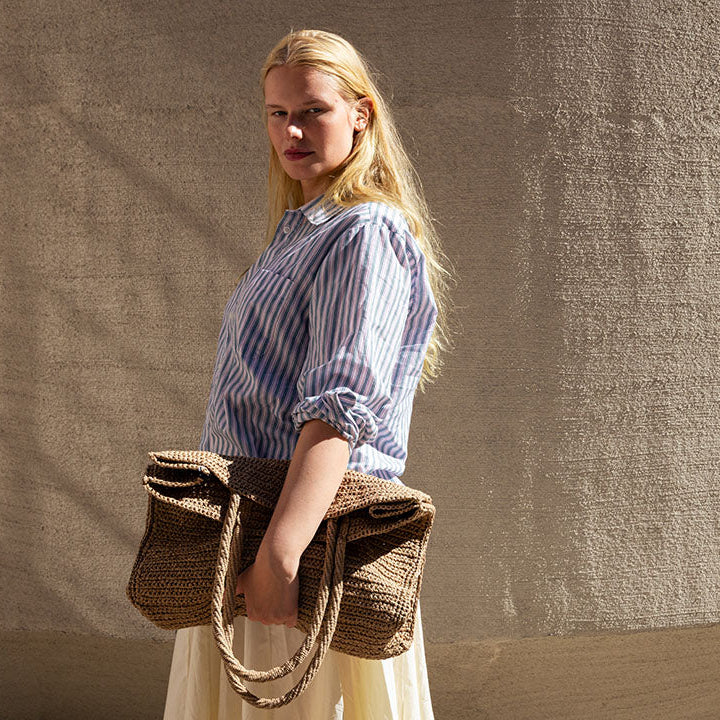 Woman holding a woven bag against a textured beige wall