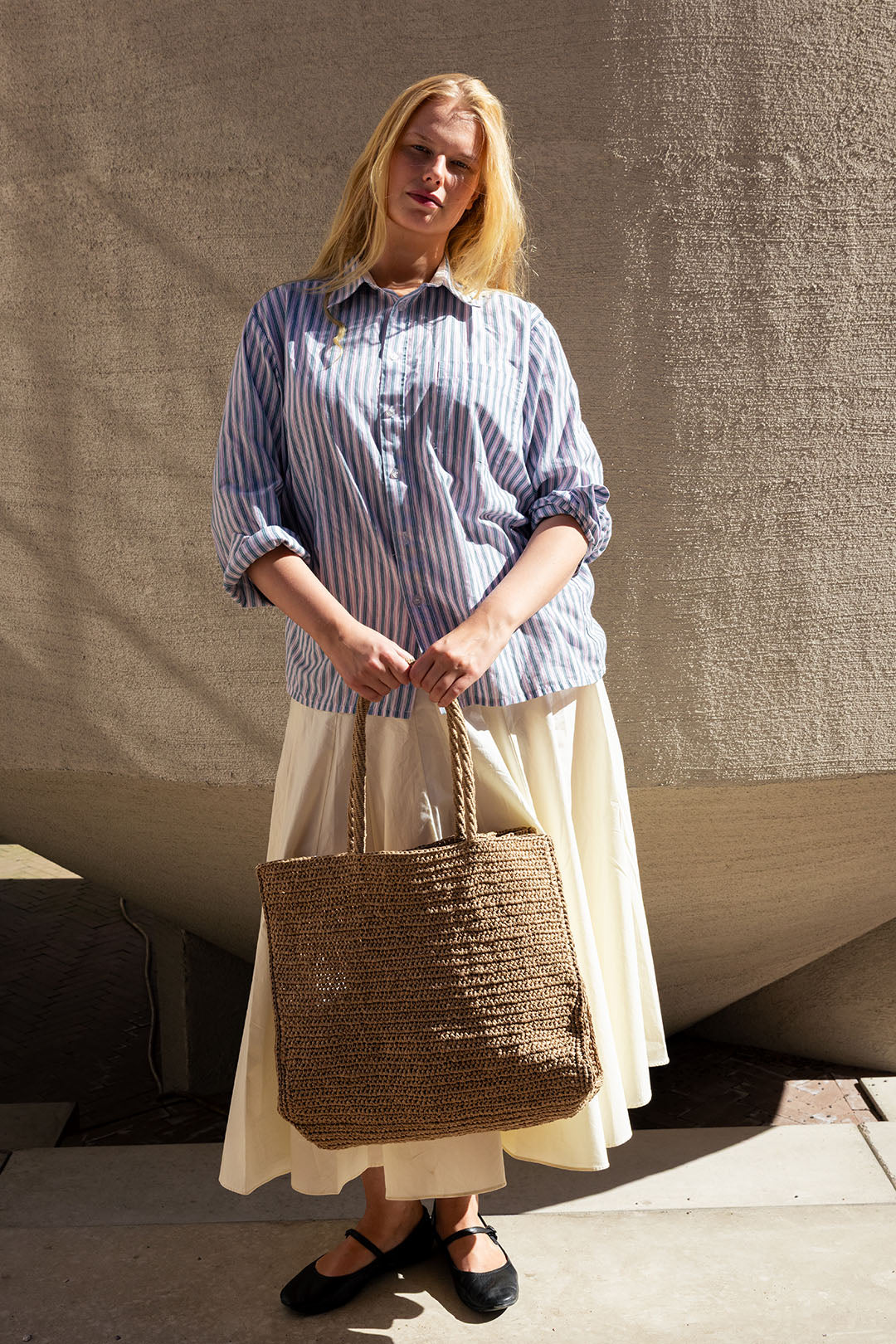Woman holding a woven bag against a textured wall.