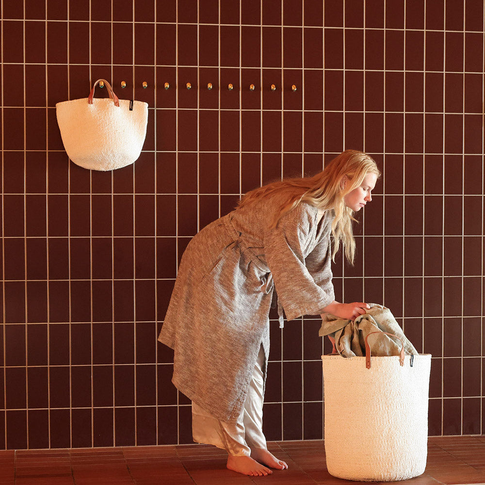 Beautiful handmade white basket with leather handles hanging on a wall hook