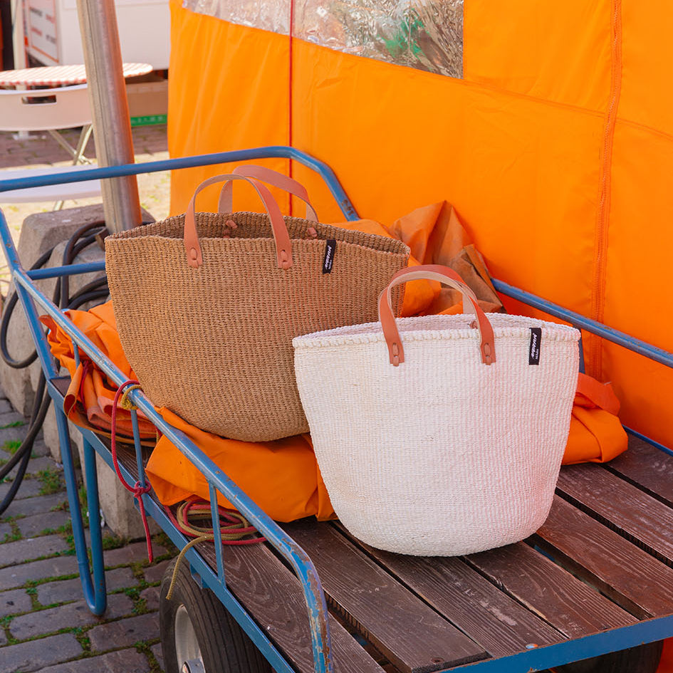 Two woven bags on a wooden cart with an orange tent in the background.