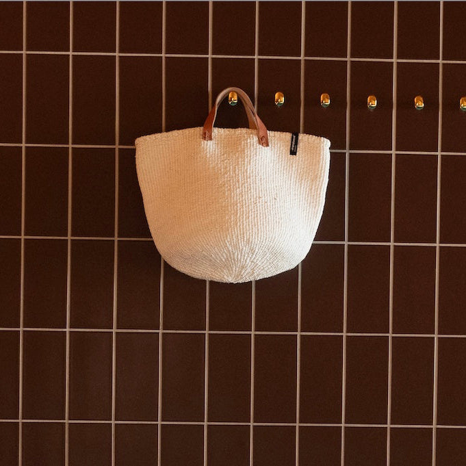Beautiful handmade white basket with leather handles hanging on a wall hook