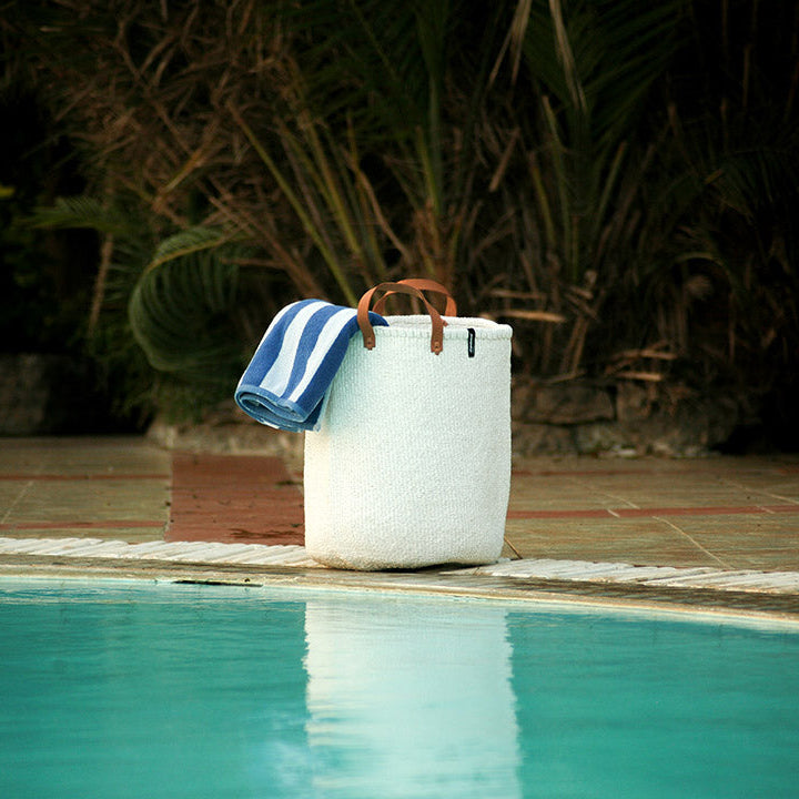 White bag with a blue towel on a poolside ledge at night.