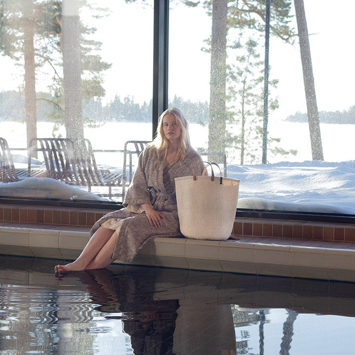 Woman sitting by a large window with a snowy landscape view, holding a white bag.
