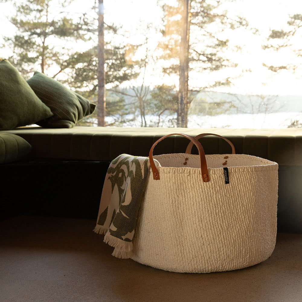Woven basket with a blanket on a carpeted floor, with a blurred natural background