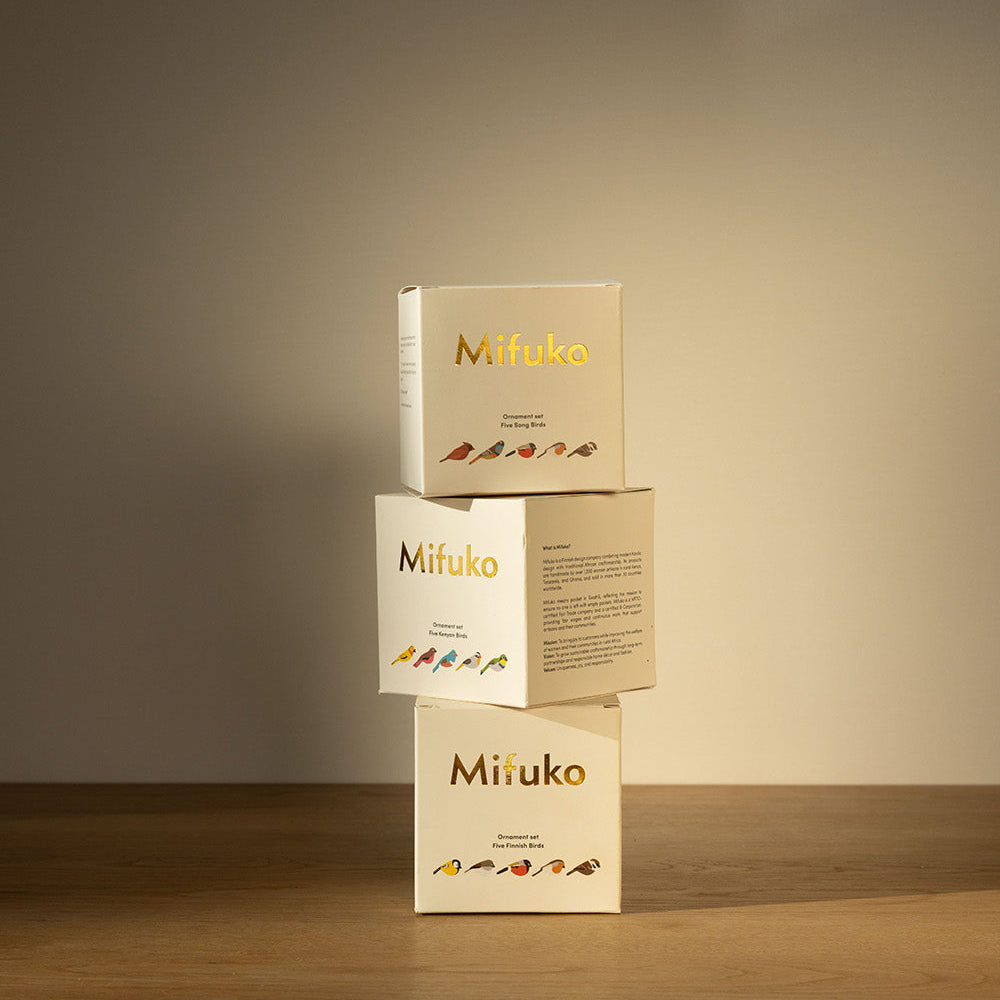 Three Mifuko bird set boxes stacked on a wooden surface with a neutral background