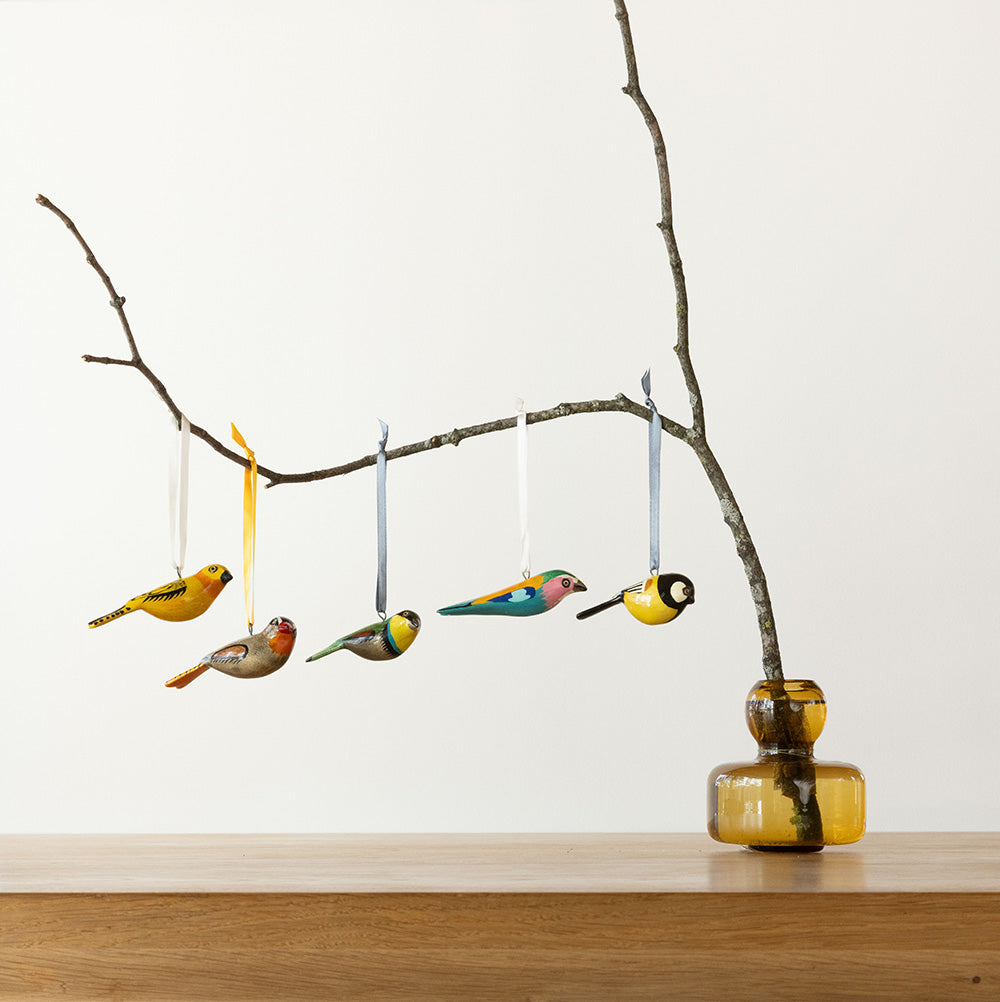 Decorative birds hanging from a branch with a vase on a wooden surface