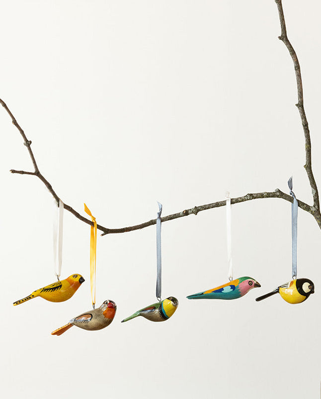 Decorative birds hanging from a branch with a vase on a wooden surface