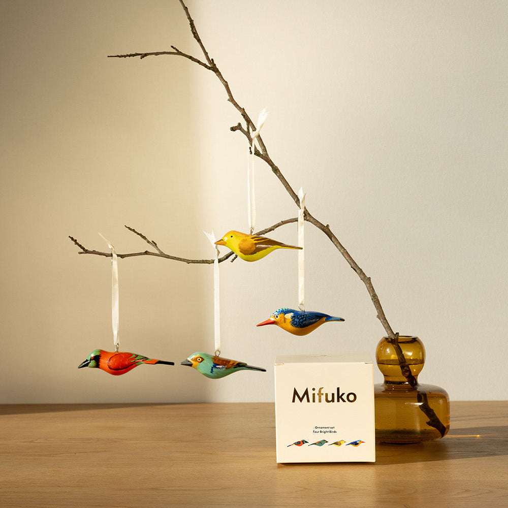 Decorative birds hanging from a branch with a Mifuko box on a wooden surface.