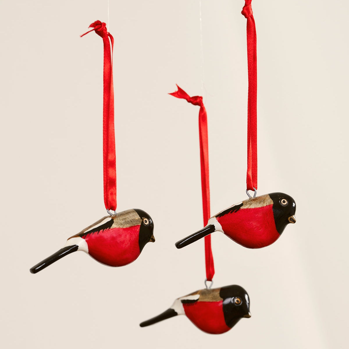 Three red bird-shaped ornaments with black heads on red ribbons against a beige background