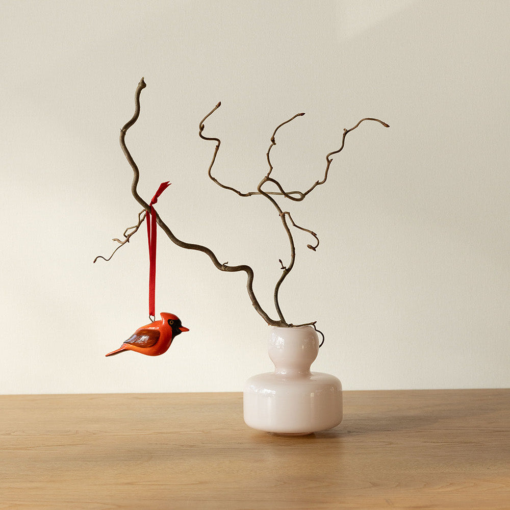 Decorative vase with branches and a small bird ornament on a wooden surface.