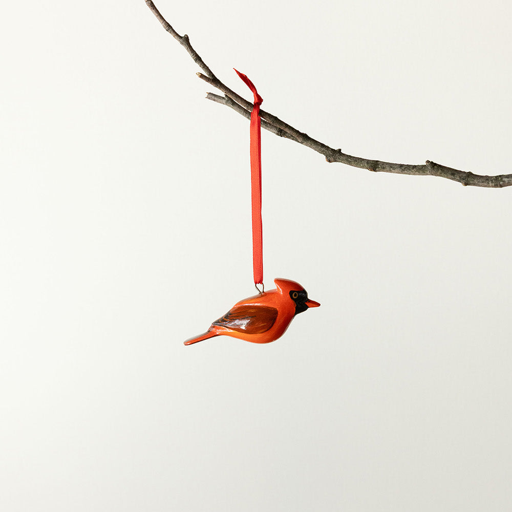 Red cardinal ornament hanging from a branch on a white background