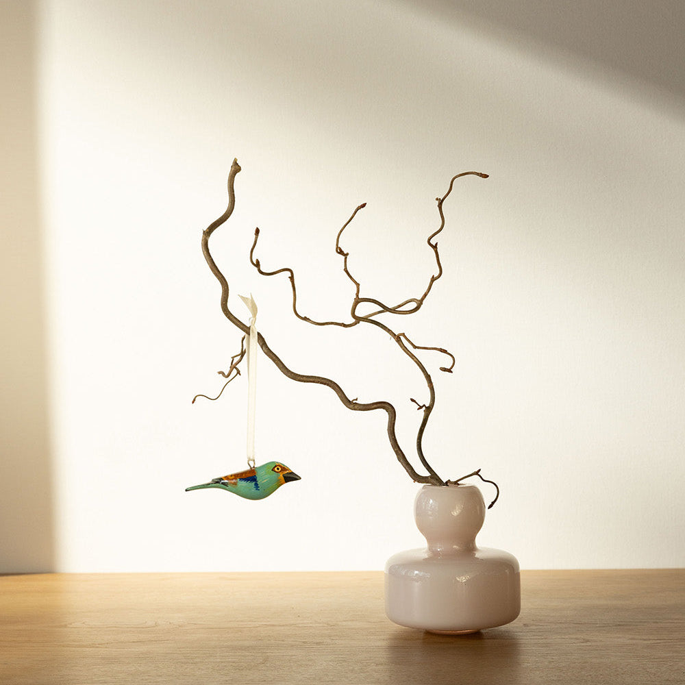 Small white vase with decorative branches and a bird figurine on a wooden surface.
