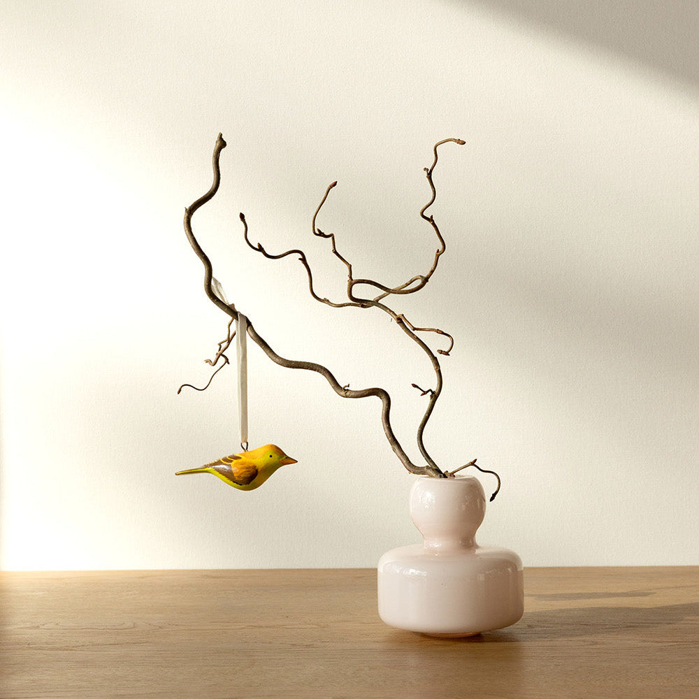 Decorative branch with a small yellow bird on a white vase against a neutral background