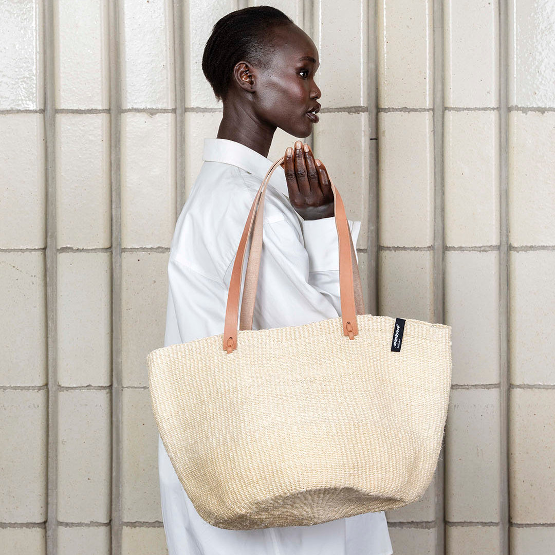 Person holding a beige tote bag against a tiled wall