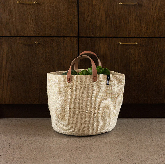 Woven basket with handles on a concrete floor in front of wooden cabinets