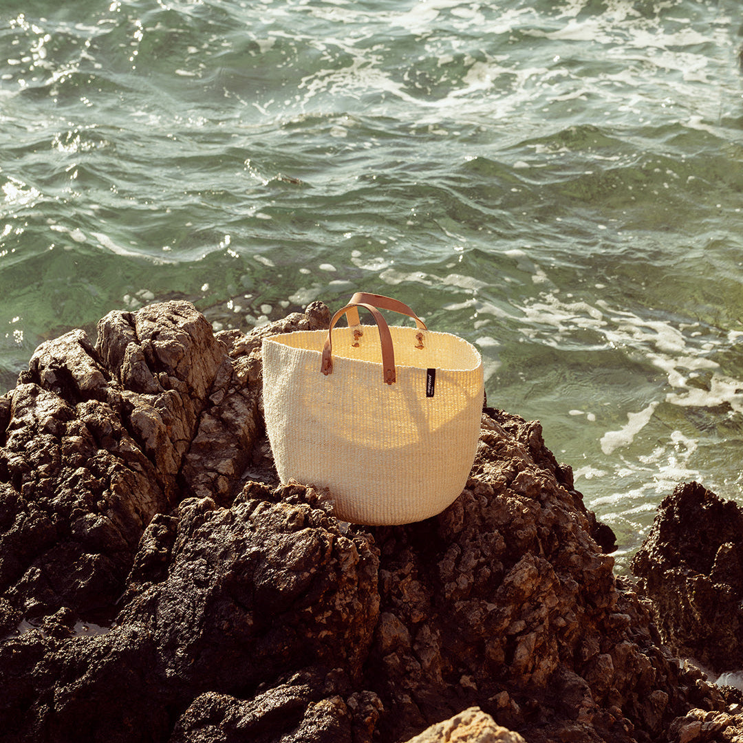 natural White sisal bag with brown handles on a rocky outcrop by the ocean