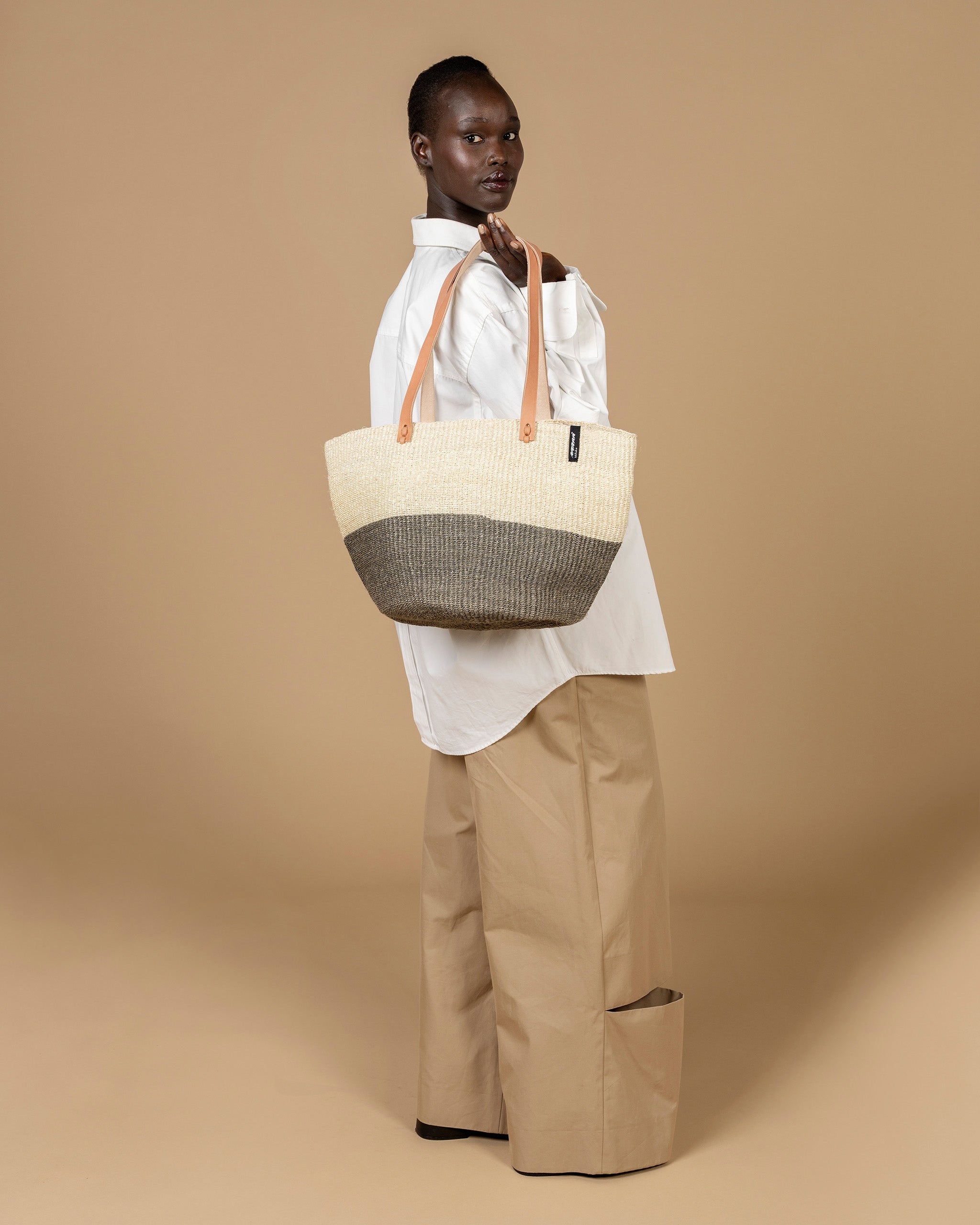 Person holding a beige tote bag with a woven pattern against a beige background