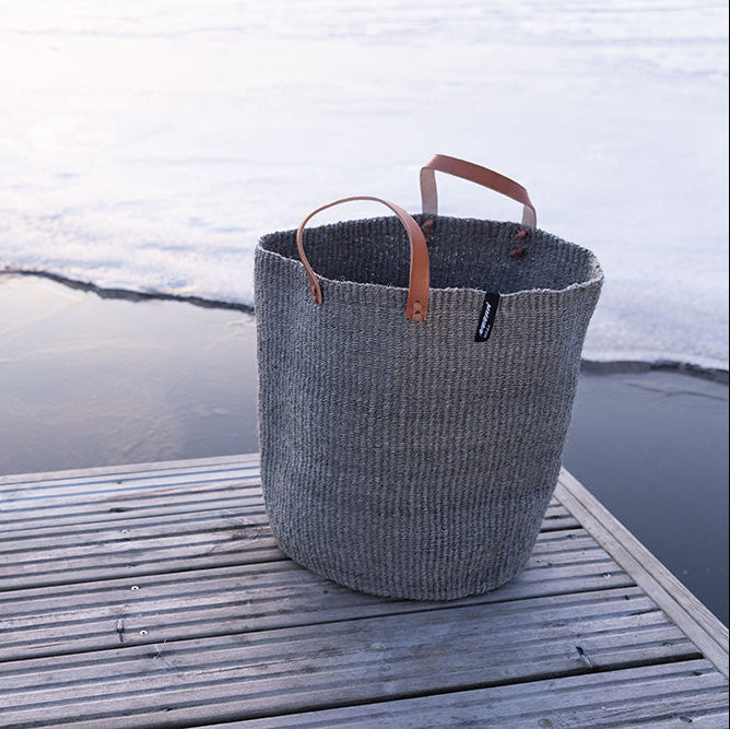 Textured basket with leather handles on a wooden dock by a body of water