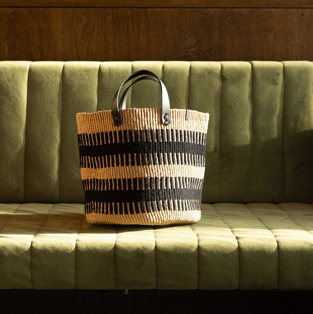 Woven bag with black patterns on a green sofa against a wooden wall.
