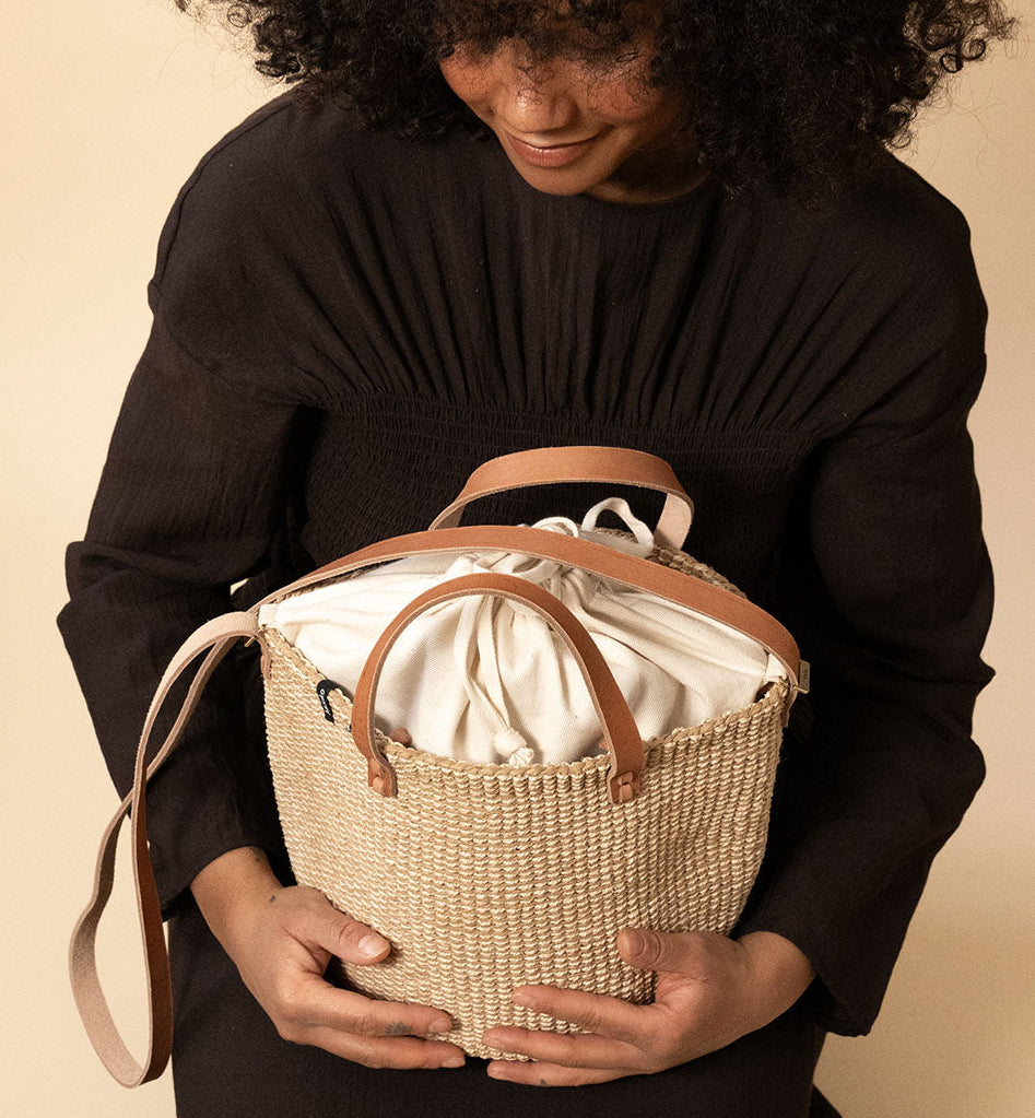 Person holding a woven basket with a beige interior against a beige background