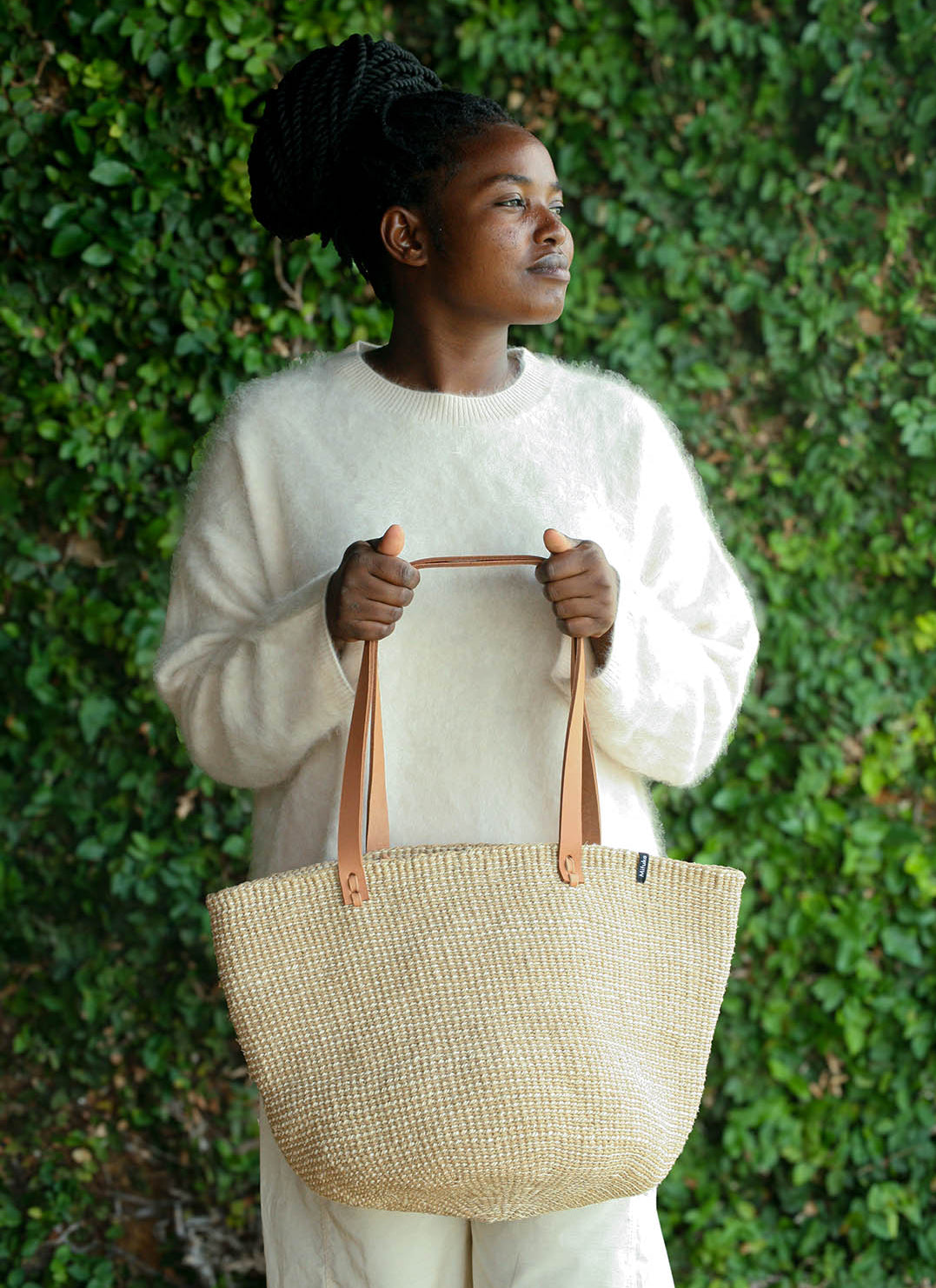 Person holding a woven bag against a green leafy background